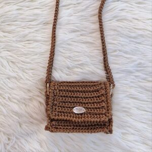 Handmade Nicky Purse in brown color, crafted from thick premium polyester yarn, featuring a compact design with a long strap, displayed on a white furry background.