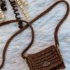 Handmade Nicky Purse in brown color, crafted from thick premium polyester yarn, featuring a compact design with a long strap, displayed on a white furry background.