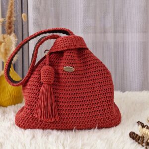 Riley Reversible Bag in a vibrant red color, handcrafted from macrame cotton yarn, displayed on a white fur surface with a tassel detail.