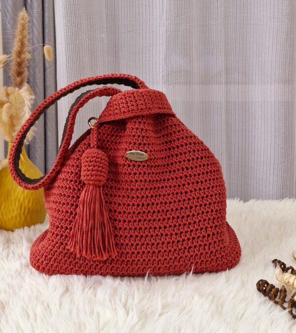 Riley Reversible Bag in a vibrant red color, handcrafted from macrame cotton yarn, displayed on a white fur surface with a tassel detail.