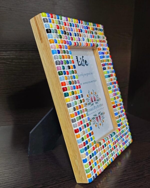 Colorful Rainbow Mosaic Frame displayed on a wooden table, featuring vibrant square tiles in various colors surrounding a 4x6 inch photo. The frame adds a lively and artistic touch to the decor.