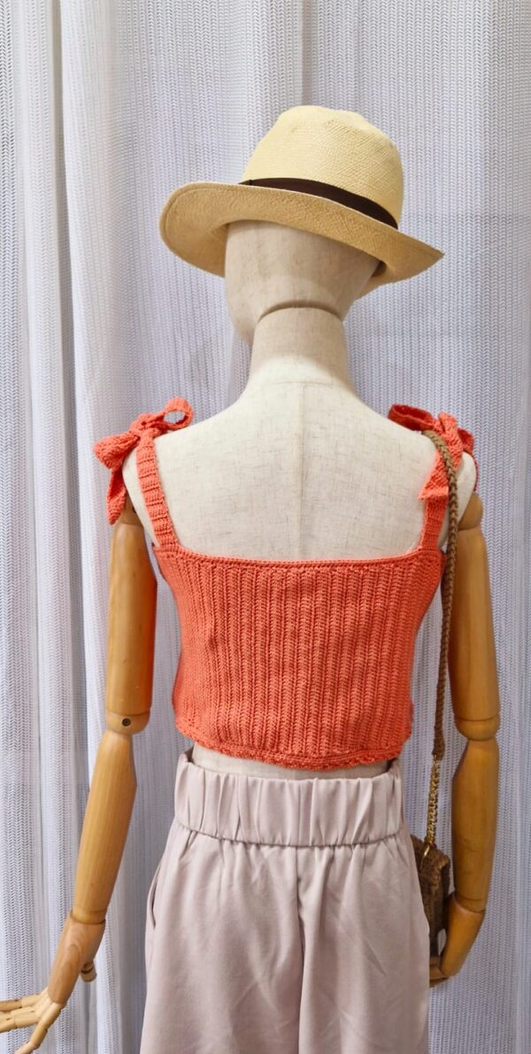 "Handmade coral-colored cotton top named 'Andrea Top' by Arty-Crafty by Vanessa, featuring adjustable shoulder ties and a square neckline, displayed on a mannequin with a straw hat and a small woven bag.