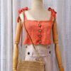 "Handmade coral-colored cotton top named 'Andrea Top' by Arty-Crafty by Vanessa, featuring adjustable shoulder ties and a square neckline, displayed on a mannequin with a straw hat and a small woven bag.