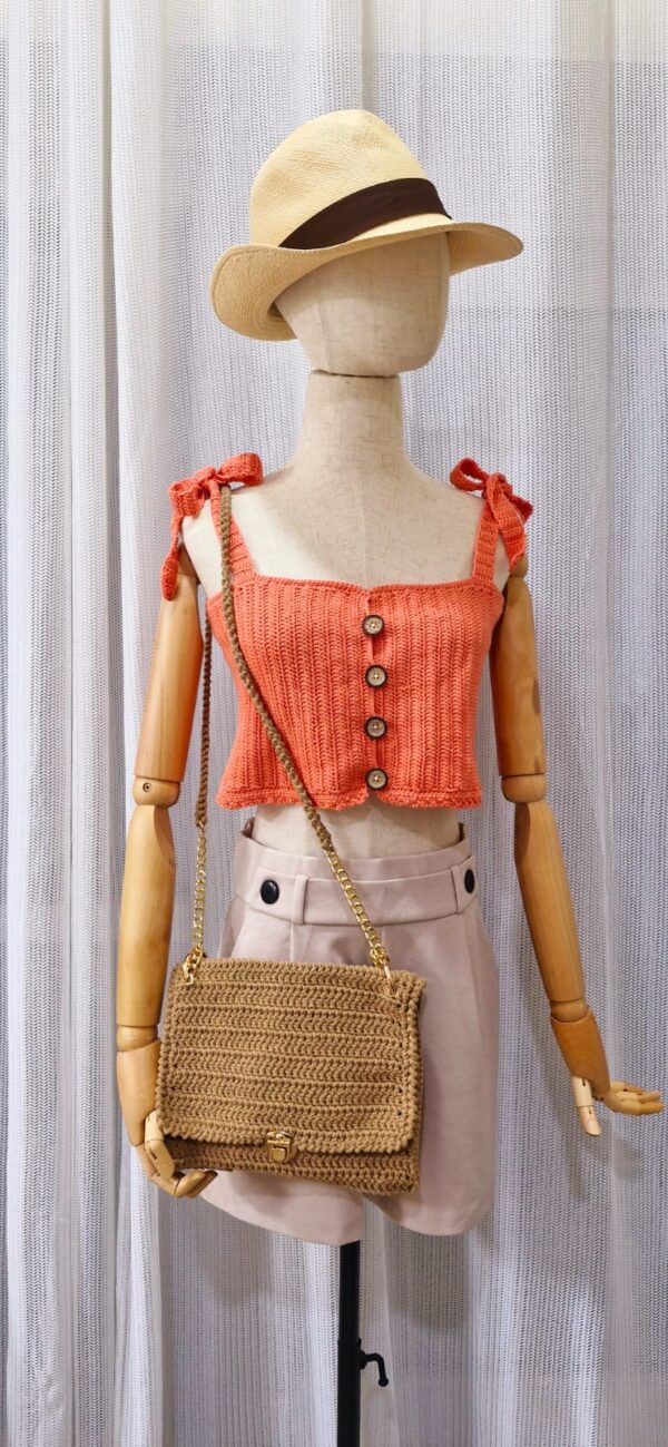 "Handmade coral-colored cotton top named 'Andrea Top' by Arty-Crafty by Vanessa, featuring adjustable shoulder ties and a square neckline, displayed on a mannequin with a straw hat and a small woven bag.