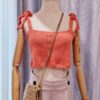 "Handmade coral-colored cotton top named 'Andrea Top' by Arty-Crafty by Vanessa, featuring adjustable shoulder ties and a square neckline, displayed on a mannequin with a straw hat and a small woven bag.