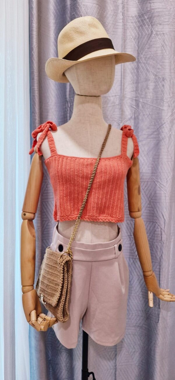 "Handmade coral-colored cotton top named 'Andrea Top' by Arty-Crafty by Vanessa, featuring adjustable shoulder ties and a square neckline, displayed on a mannequin with a straw hat and a small woven bag.