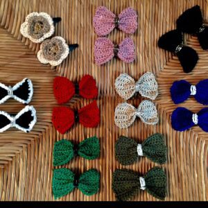 Handmade crochet hair clips named 'Riah Hair Clip' by Arty-Crafty by Vanessa, featuring colorful bows and flowers made from cotton yarn, arranged in pairs on a textured wooden surface.