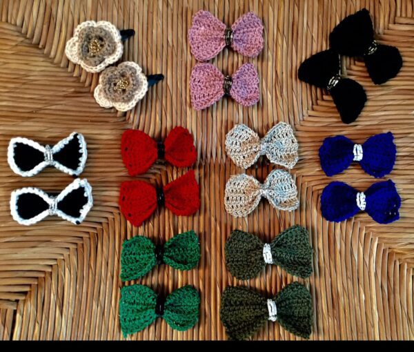 Handmade crochet hair clips named 'Riah Hair Clip' by Arty-Crafty by Vanessa, featuring colorful bows and flowers made from cotton yarn, arranged in pairs on a textured wooden surface.