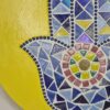 Handcrafted Evil Eye Hamsa Hand Mosaic, featuring a vibrant yellow background and intricate blue and multicolored mosaic tiles forming the protective Hamsa symbol