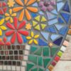 Handcrafted heart-shaped mosaic wall art featuring colorful glass tiles arranged in a vibrant floral pattern, with a basket of flowers at the center. The mosaic is designed with a mix of bright reds, yellows, oranges, blues, greens, and purples, creating a cheerful and lively decoration