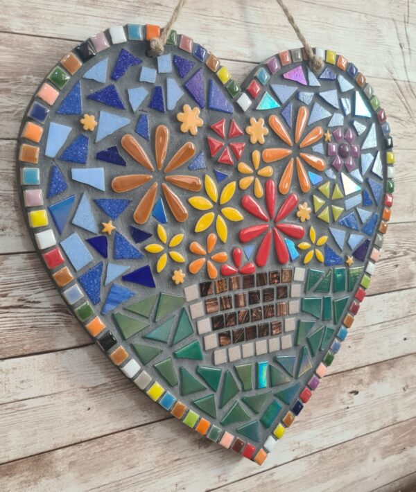 Handcrafted heart-shaped mosaic wall art featuring colorful glass tiles arranged in a vibrant floral pattern, with a basket of flowers at the center. The mosaic is designed with a mix of bright reds, yellows, oranges, blues, greens, and purples, creating a cheerful and lively decoration