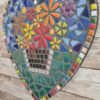 Handcrafted heart-shaped mosaic wall art featuring colorful glass tiles arranged in a vibrant floral pattern, with a basket of flowers at the center. The mosaic is designed with a mix of bright reds, yellows, oranges, blues, greens, and purples, creating a cheerful and lively decoration