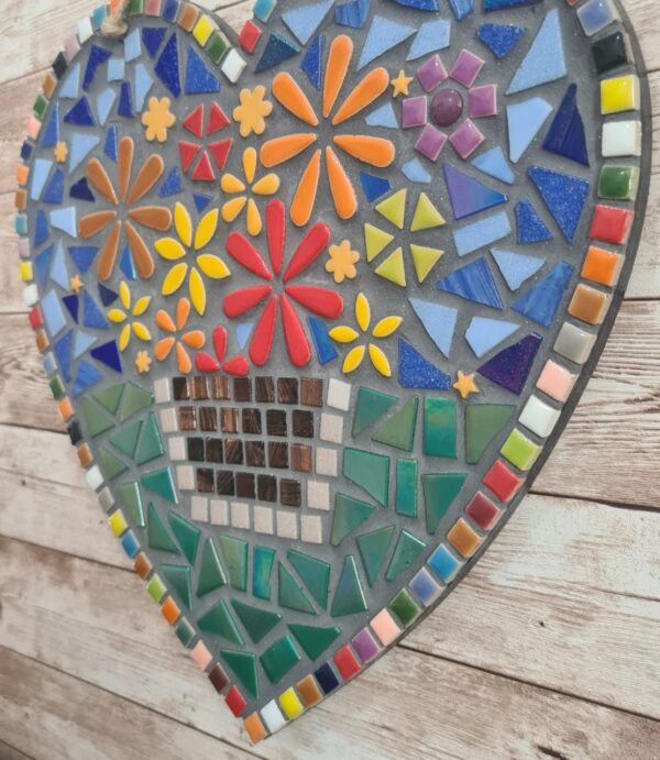 Handcrafted heart-shaped mosaic wall art featuring colorful glass tiles arranged in a vibrant floral pattern, with a basket of flowers at the center. The mosaic is designed with a mix of bright reds, yellows, oranges, blues, greens, and purples, creating a cheerful and lively decoration