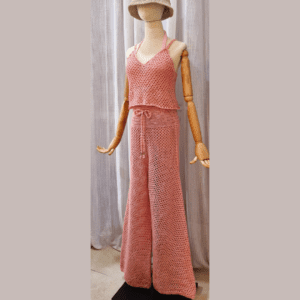 Handmade crochet Charmaine Set in a blush pink tone, featuring a sleeveless crop top and wide-leg pants made from a cotton-acrylic blend. The set is shown on a wooden mannequin with a beige crochet bucket hat, offering a casual yet elegant look.