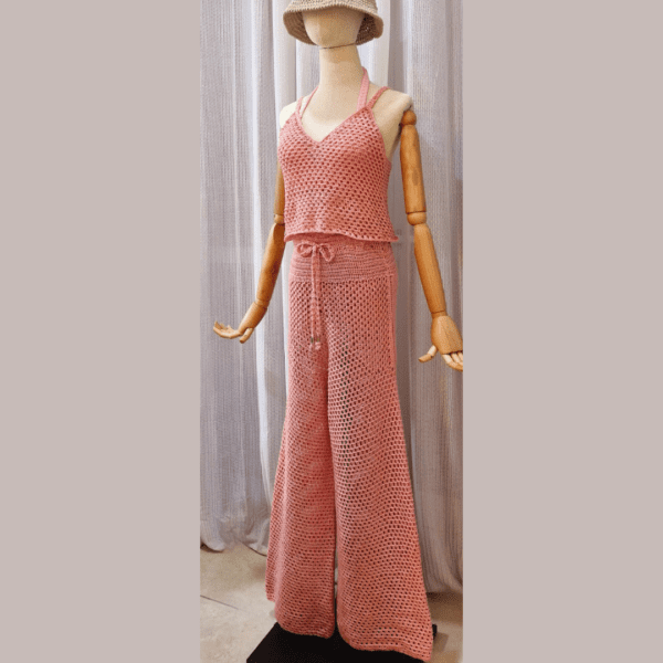 Handmade crochet Charmaine Set in a blush pink tone, featuring a sleeveless crop top and wide-leg pants made from a cotton-acrylic blend. The set is shown on a wooden mannequin with a beige crochet bucket hat, offering a casual yet elegant look.