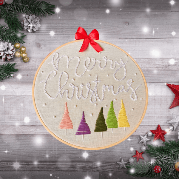 Hand-embroidered "Merry Christmas" wall art featuring colorful Christmas trees, framed in an 8-inch wooden hoop with a red ribbon, created by Anu Paulson.