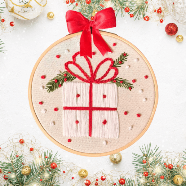 Hand-embroidered wall art featuring a festive Christmas gift, framed in an 8-inch wooden hoop with a red bow, created by Anu Paulson.