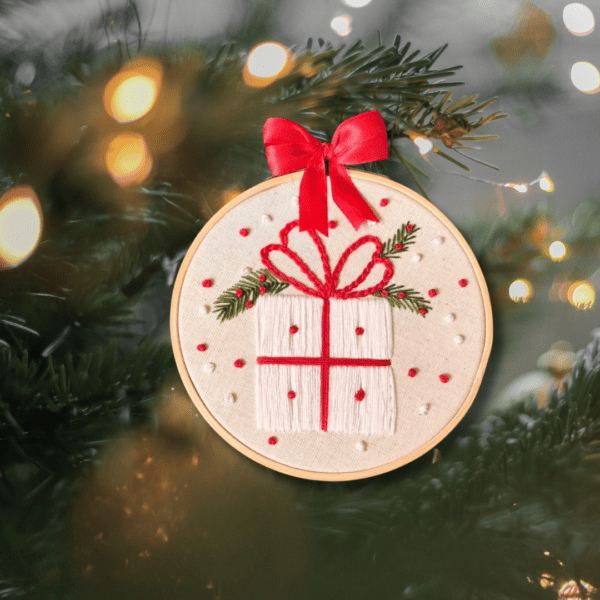 Hand-embroidered wall art featuring a festive Christmas gift, framed in an 8-inch wooden hoop with a red bow, created by Anu Paulson.