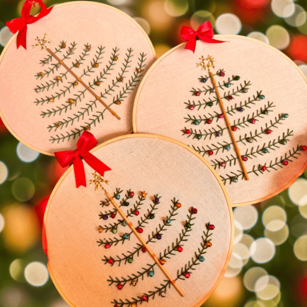 Hand-embroidered Christmas tree wall art with colorful ornaments, framed in a 5-inch wooden hoop with a red bow, created by Anu Paulson.