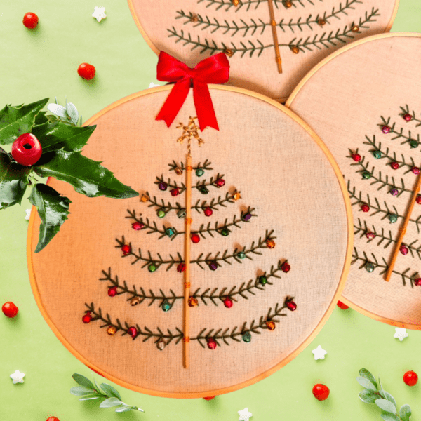 Hand-embroidered Christmas tree wall art with colorful ornaments, framed in a 5-inch wooden hoop with a red bow, created by Anu Paulson.