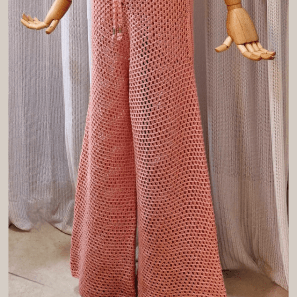 Handmade crochet Charmaine Set in a blush pink tone, featuring a sleeveless crop top and wide-leg pants made from a cotton-acrylic blend. The set is shown on a wooden mannequin with a beige crochet bucket hat, offering a casual yet elegant look.