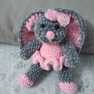 Handmade bunny plushie made with soft gray and pink velvet yarn, featuring floppy ears, a pink bow, and an adorable outfit. Perfect for babies and toddlers as a soft toy or baby shower gift.