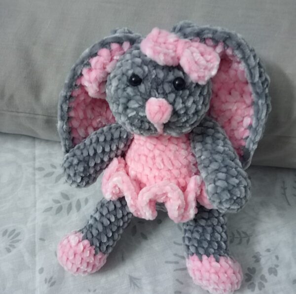 Handmade bunny plushie made with soft gray and pink velvet yarn, featuring floppy ears, a pink bow, and an adorable outfit. Perfect for babies and toddlers as a soft toy or baby shower gift.