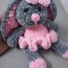 Handmade bunny plushie made with soft gray and pink velvet yarn, featuring floppy ears, a pink bow, and an adorable outfit. Perfect for babies and toddlers as a soft toy or baby shower gift.