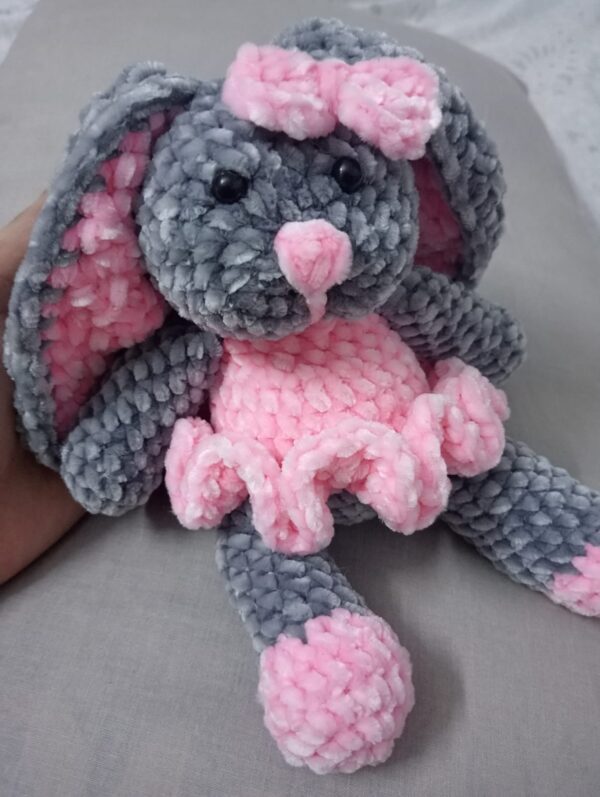 Handmade bunny plushie made with soft gray and pink velvet yarn, featuring floppy ears, a pink bow, and an adorable outfit. Perfect for babies and toddlers as a soft toy or baby shower gift.