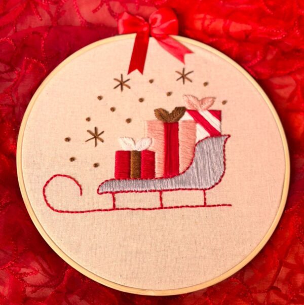 Hand-embroidered wall art featuring a Christmas sleigh filled with gifts, framed in an 8-inch wooden hoop with a festive red bow, created by Anu Paulson.