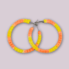 Handmade macrame earrings in bright yellow and orange, circular hoop design by Rita Lewis.