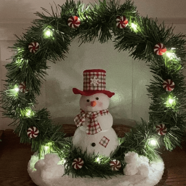 Snowman holiday decoration with LED lights and peppermint accents on a wooden base.