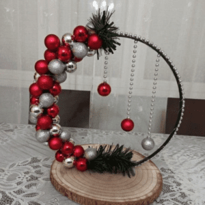 Crescent-shaped holiday ornament decoration with red and silver baubles on a wooden base.