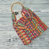 Multicolor handwoven macrame bag with wooden handle, zipper closure, and cotton lining, 12 inches wide and 18 inches long.