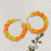 Handmade twisted macrame earrings in marigold shades of yellow and orange, circular hoop design by Rita Lewis.