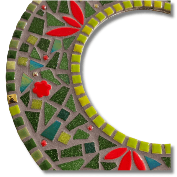 A handcrafted round Christmas Mosaic Mirror adorned with red and green ceramic and glass tiles, featuring a festive bow, pinecone, and bell decoration. Sealed in grey, 30 cm in diameter. Perfect for holiday décor.