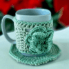 Handmade Blissful Brew Set featuring a crochet mug cover and matching coaster. Customizable colors include blue, red, green, and festive patterns. A perfect gift for tea and coffee lovers.