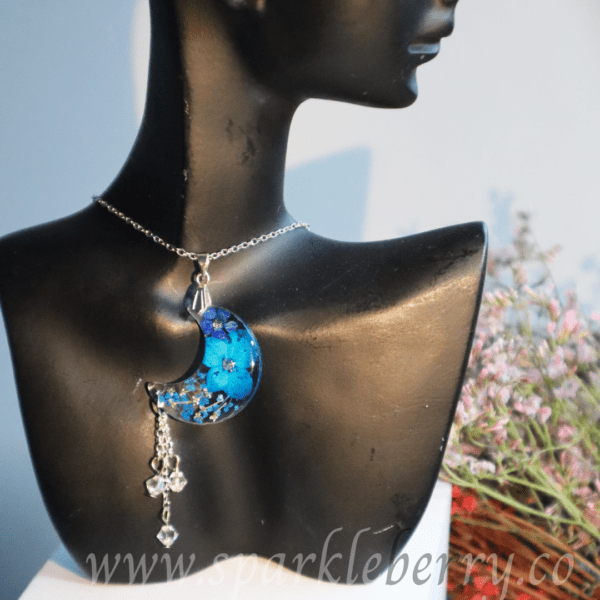 Handcrafted crescent moon pendant necklace with dried flowers encased in resin, dangling Swarovski beads, and a silver-tone chain, measuring 7 cm with tassel and bail.