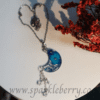 Handcrafted crescent moon pendant necklace with dried flowers encased in resin, dangling Swarovski beads, and a silver-tone chain, measuring 7 cm with tassel and bail.