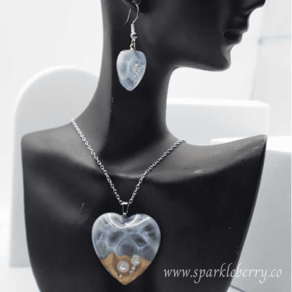 Heart-shaped jewelry set featuring a blue resin pendant with pearls and golden sand, paired with matching earrings, lightweight and ocean-inspired.