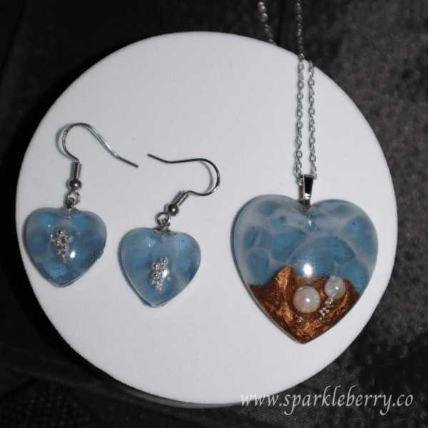 Heart-shaped jewelry set featuring a blue resin pendant with pearls and golden sand, paired with matching earrings, lightweight and ocean-inspired.