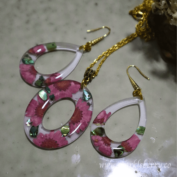 Floral resin jewelry set featuring pressed pink flowers and abalone shells in hypoallergenic earrings and a gold-plated pendant.