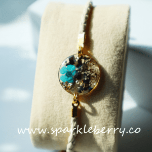 Adjustable leather bracelet with a 2cm resin centerpiece featuring dried flowers, gold flakes, and blue accents, with gold-plated details