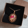 Handcrafted pendant with vibrant dried flowers and gold flakes encased in resin, set in a vintage-style filigree frame with a gold-plated chain.