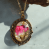 Handcrafted pendant with vibrant dried flowers and gold flakes encased in resin, set in a vintage-style filigree frame with a gold-plated chain.