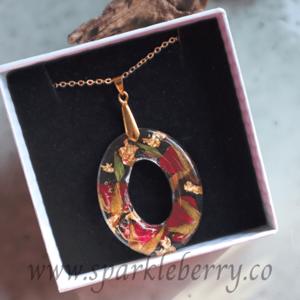 Handcrafted oval pendant with real dried roses and gold flakes encased in resin, featuring a gold-plated stainless steel chain, displayed in an elegant gift box.