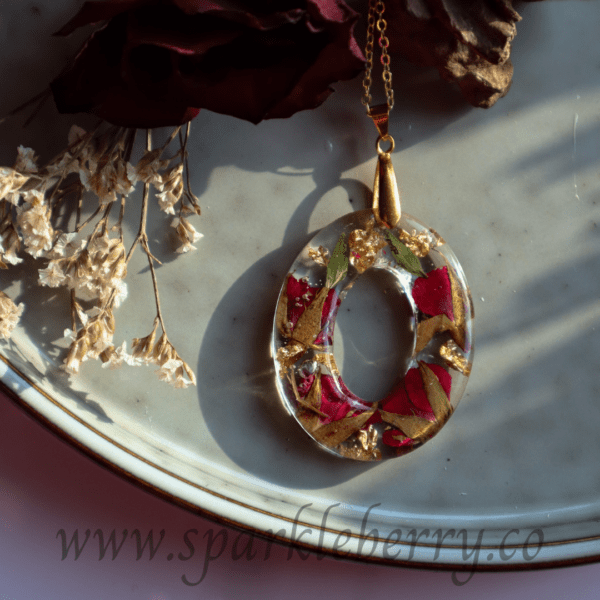 Handcrafted oval pendant with real dried roses and gold flakes encased in resin, featuring a gold-plated stainless steel chain, displayed in an elegant gift box.