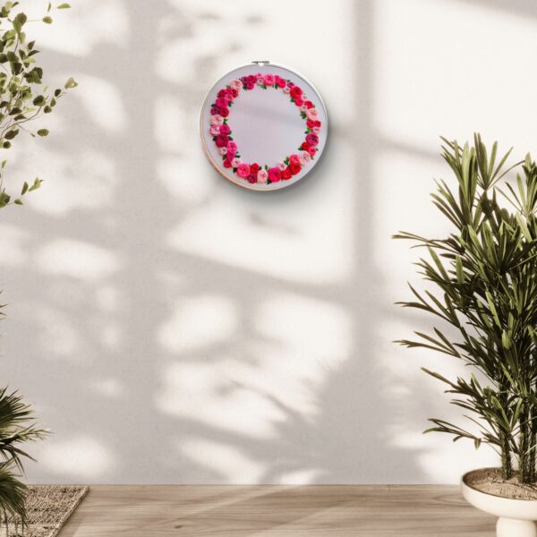 Hand-embroidered floral wreath wall art featuring pink, red, and blush roses with green leaves, framed in a 10-inch wooden hoop, created by Anu Paulson.