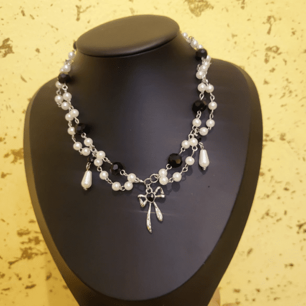 Handmade black and pearl beaded necklace featuring a silver bow charm, crafted by Nel's Jewels.