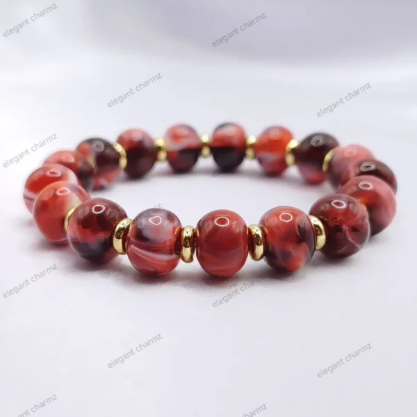 Handmade red ceramic bead bracelet with gold-plated spacer beads, displayed on a white surface.